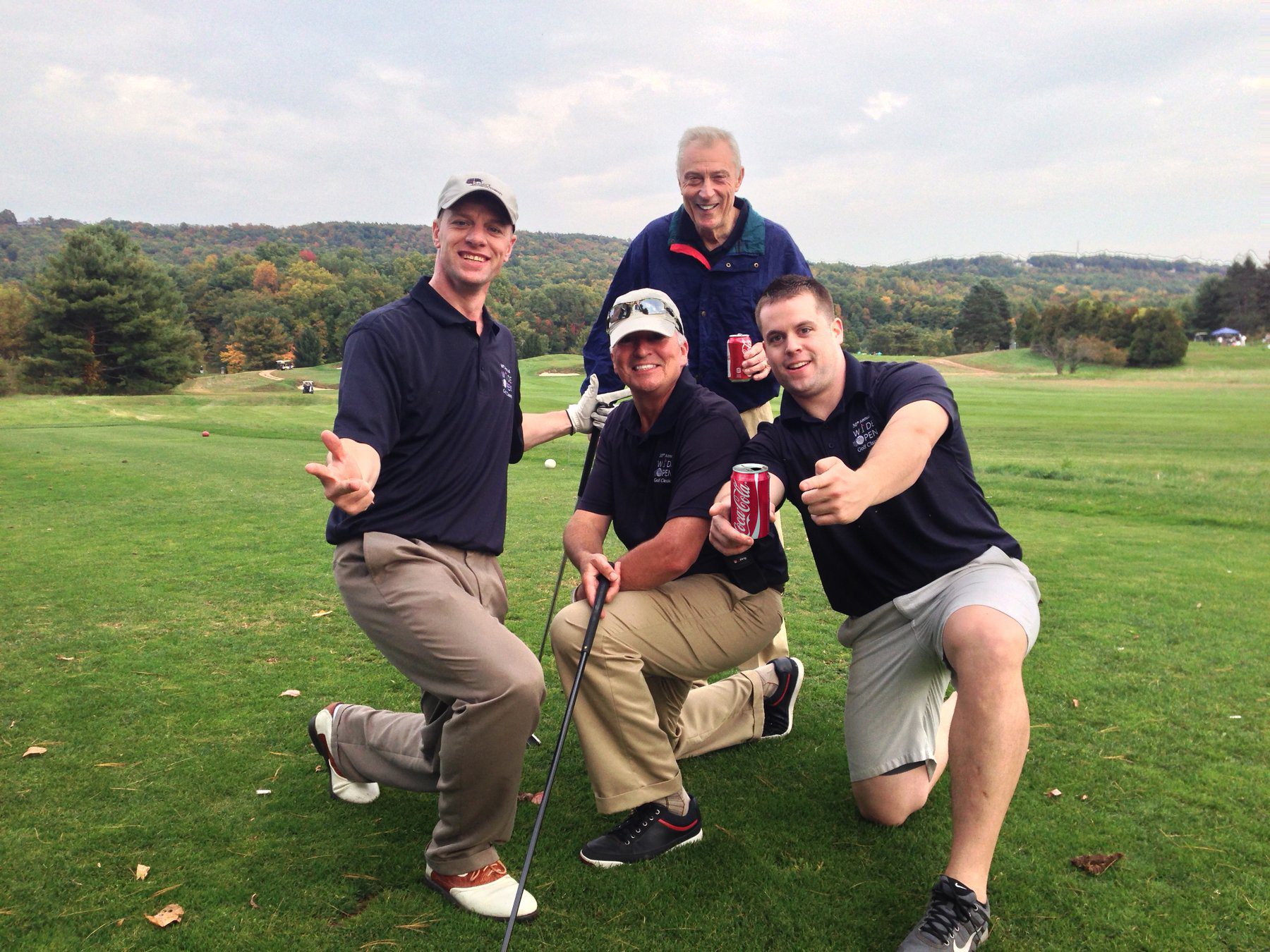 Four golfers kneeling together on the fairway at the Wide Open Golf Classic